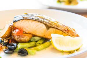 A plate of food with a lemon wedge and a piece of fish photo