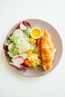 A plate with a croissant, salad and a side of dressing photo