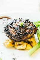 A steak with vegetables and sauce on a white plate photo