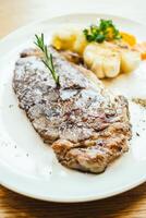 A steak on a white plate with potatoes and vegetables photo