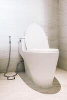 A white toilet with a seat and a hose photo