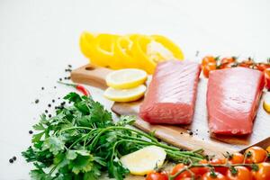 Raw tuna, lemon, tomatoes and herbs on a cutting board photo