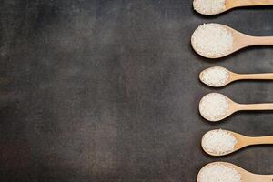 Six wooden spoons with rice in them on a black background photo