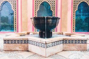 A fountain in a courtyard with a pink building in the background photo