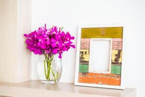 A vase of purple orchids sits next to a wooden frame photo