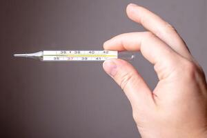 Hand holds a medical mercury thermometer with normal temperature, on a gray background. photo