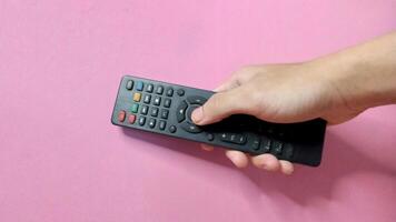 Close up of a hand using a black TV remote control against a pink background. Concept of entertainment, technology, and leisure. photo