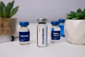 antibiotics and some vaccines in vials, placed on a white table with artificial plant decoration. medical concepts photo