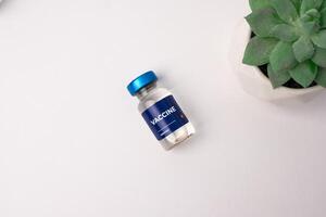 a vaccine lying on a white table with an ornamental plant in the corner. health and medical concepts photo