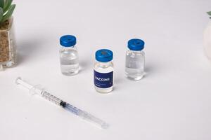 top view of some vaccines and a syringe with artificial flowers on a table, inside a clinic room. health and medical concepts photo