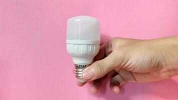 Energy efficient LED light bulb in hand against pink background. Concept of sustainability, technology, and innovation. photo