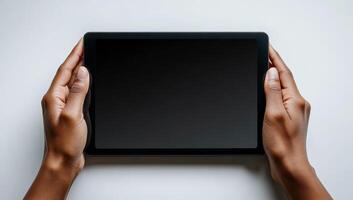 A person is holding a tablet with a black screen. The tablet is not turned on, and the person is holding it in their hands photo