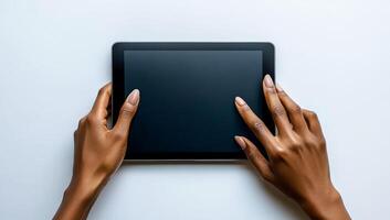 A person is holding a tablet with their hands. The tablet is black and has no screen. The person is looking at the tablet with a serious expression photo