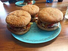 Three homemade hamburgers sit on a decorative blue plate. Each burger features a sesame seed bun, grilled meat, and an assortment of fresh vegetables, embodying a delightful meal experience photo