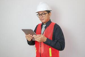 Smiling excited young Asian architect engineer employee man in a formal shirt helmet pointing finger at tablet isolated on white background. People work on architecture project photo