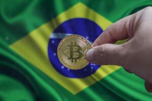 Hand of a man with a gold bitcone Cryptocurrency Digital bit of coins in a hand on a background of the flag of Brazil. photo