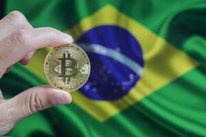 Hand of a man with a gold bitcone Cryptocurrency Digital bit of coins in a hand on a background of the flag of Brazil. photo