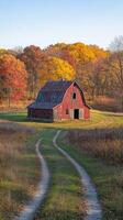 A rustic red barn stands alone on a winding path, framed by vibrant autumn trees under clear skies. photo