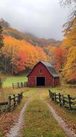 A red barn at the end of a dirt path is framed by colorful fall trees beneath a cloudy sky. photo