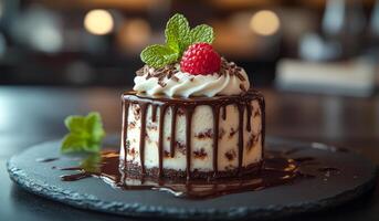 A chocolate cake with a green leaf on top and a red raspberry on the side. The cake is sitting on a black plate photo