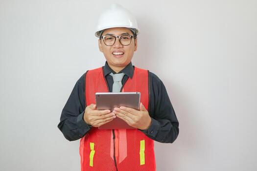 un hermoso masculino ingeniero o arquitecto con un blanco casco. masculino ingeniero en pie con tableta mirando a cámara sonriente contento en blanco antecedentes en un foto estudio.