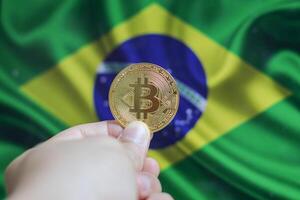 Hand of a man with a gold bitcone Cryptocurrency Digital bit of coins in a hand on a background of the flag of Brazil. photo