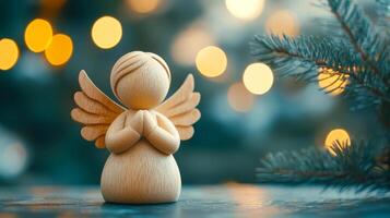 A wooden angel is sitting on a table with a tree branch in the background. The angel is holding its hands together in a prayer position. The scene has a peaceful and serene mood photo