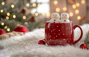 Two snowmen in a red mug with marshmallows. The snowmen are sitting in the mug and the mug is on a white blanket photo