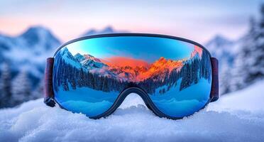 A pair of goggles with a blue lens and a reflection of the mountains in the mirror. The goggles are on top of a snowy surface photo