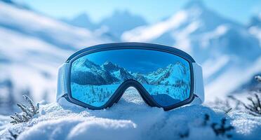 A pair of goggles with a blue lens sits on a snowy surface. The scene is set in a mountainous area, with snow-covered trees in the background. The goggles are the main focus of the image photo