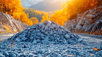 Pile of gravel along a forest road in autumn light. A large mound of gravel sits beside a winding road surrounded by vibrant autumn foliage in the soft evening light. photo