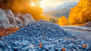 Autumn road sunset with gravel pile. A gravel mound rests by a winding road surrounded by colorful autumn trees as the sun sets in the mountains. photo