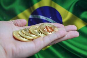 Hand of a man with a gold bitcone Cryptocurrency Digital bit of coins in a hand on a background of the flag of Brazil. photo