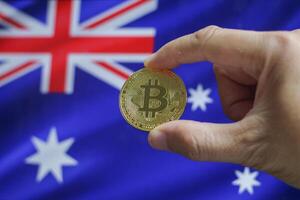 Hand of a man with a gold bitcone Cryptocurrency Digital bit of coins in a hand on a background of the flag of Australia photo