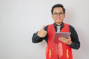 Young handsome chinese architect man wearing safety helmet and tie over yellow background doing happy thumbs up gesture with hand. Approving expression looking at the camera showing success. photo