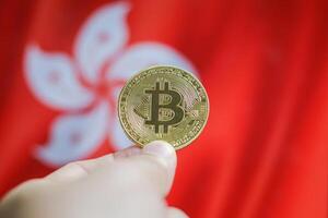 Hand of a man with a gold bitcone Cryptocurrency Digital bit of coins in a hand on a background of the flag of Hong Kong. photo
