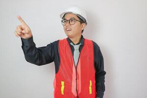 architecture, construction business and people concept - smiling asian male architect in helmet pointing finger to something over grey background photo