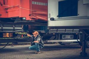 Worker Inspecting Semi Truck Trailer Connection During Daytime at a Transport Yard photo