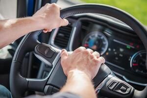 Truck Driver Gripping Steering Wheel While Navigating on a Sunny Day With Green Surroundings photo