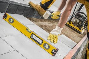 Worker Using a Level Tool to Ensure Evenness While Laying Pavers on a Construction Site photo