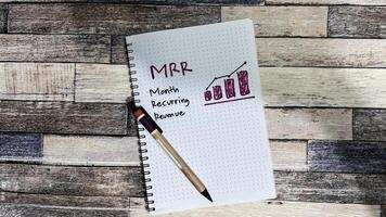 Concept of MRR - Month Recurring Revenue write on book isolated on Wooden Table. photo