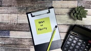 Concept of Debt vs Equity write on sticky notes isolated on Wooden Table. photo