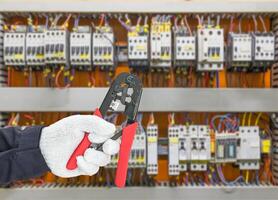 Hand in glove holding wire stripper with control panel cabinet photo