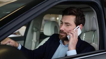 Caucasian happy man successful businessman talking mobile phone buyer smartphone call sitting new car indoors laugh auto rent service communicate vehicle luxury male guy automobile conversation salon video