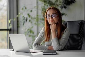 Senior chic woman using laptop at home while taking notes in notebook. Old freelancer works in the living room on a laptop while drafting details on a book. photo