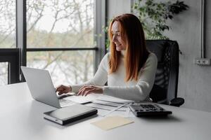 Happy, sophisticated, and elderly woman taking notes while working remotely from home. smiling middle-aged business woman watching webinar on computer. photo