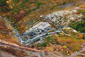 Whispers of Autumn A Serene Stream Flowing Through Vibrant Rocky Terrain photo