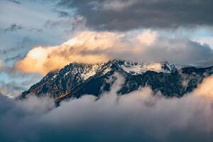 Majestic Peaks Shrouded in Wispy Clouds A Serene Winter Landscape of Snow-Capped Mountains bathed in Soft Light and Ethereal Mist. photo