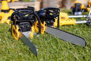 A Trio of Power Gleaming Chainsaws Resting on Lush Green Grass, Ready to Conquer Natures Challenges. Their Metallic Blades Reflecting the Serenity of the Natural World Around Them. photo
