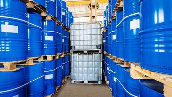 Rows of blue metal barrels and oversized plastic containers rest on sturdy pallets, echoing the organized chaos of a bustling warehouse, ready for action beneath flickering fluorescent lights photo